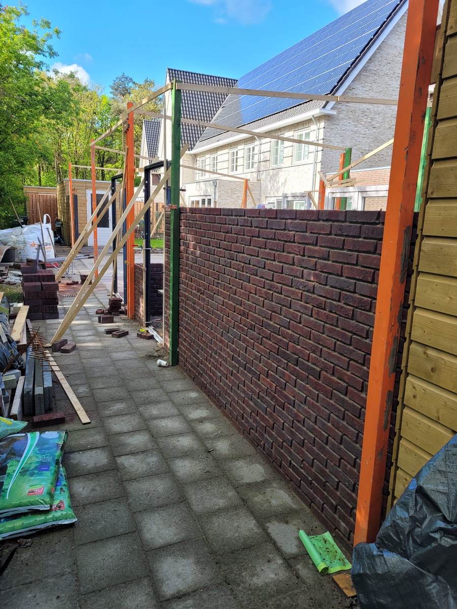 Gemetselde tuinmuur in donkere baksteen bij een woning in Helmond