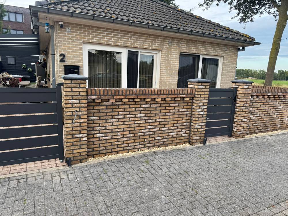Gemetselde tuinmuur met poeren, rollaag en aluminium poorten bij een woning